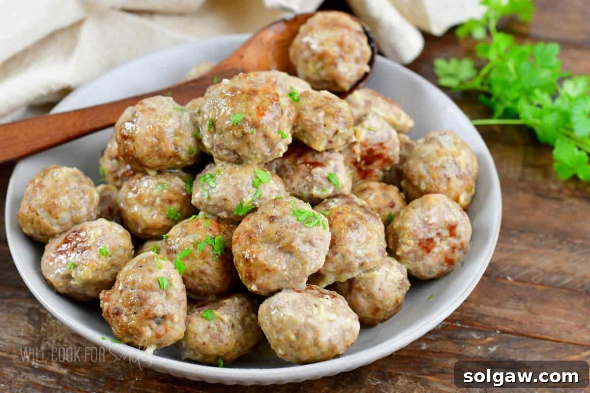 A bowl full of baked meatballs and a spoon holding one.