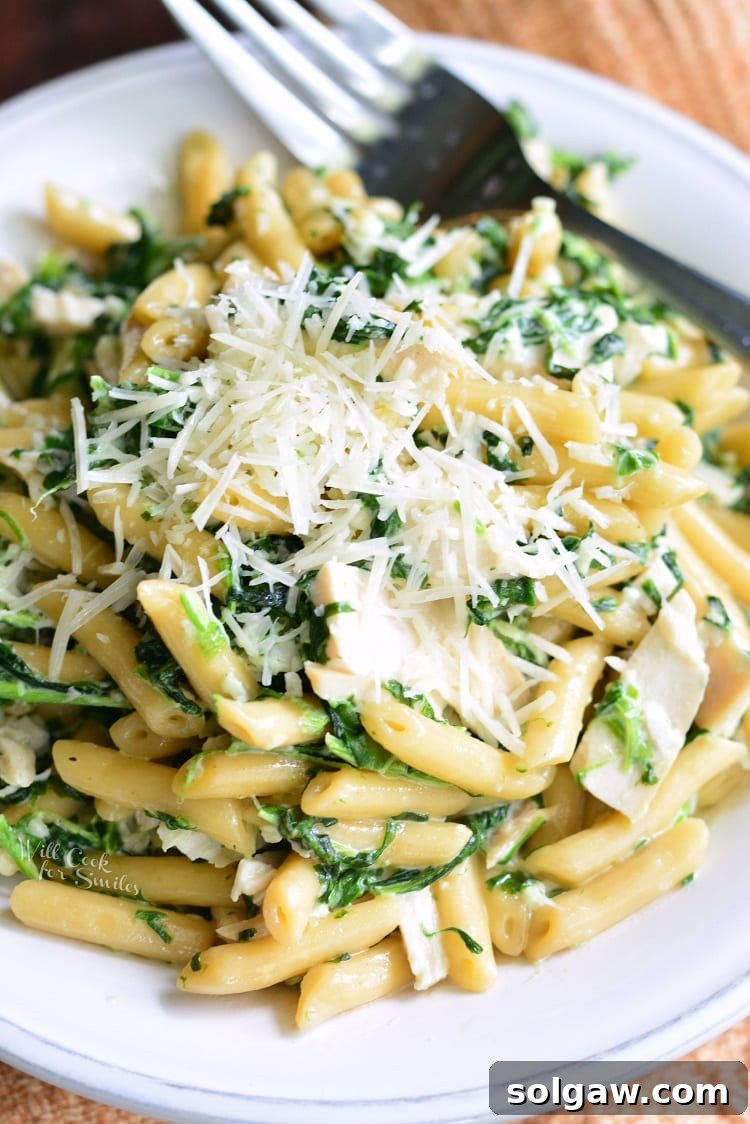 Garlic and Spinach Alfredo Chicken Pasta in a bowl with shredded cheese on top with fork 