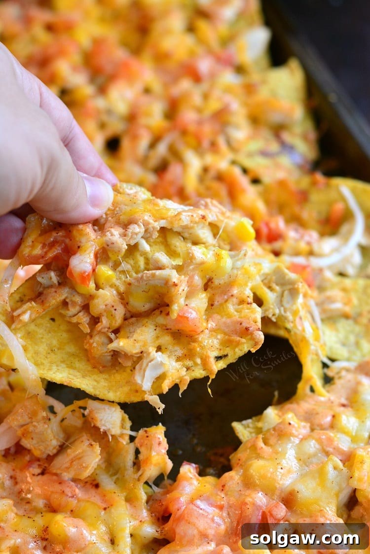 Holding a nacho in my hand with the sheet pan of nachos in the background.