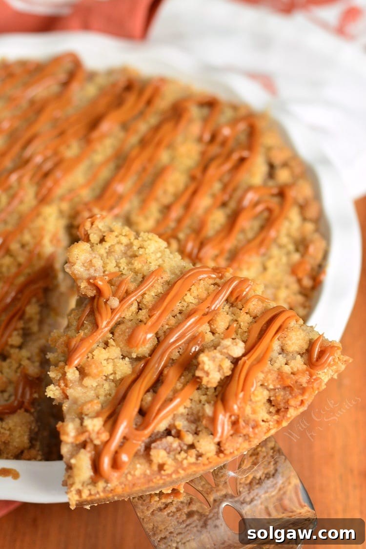 A stunning top-down view of the Caramel Apple Cookie Crust Pie, with a perfectly cut piece being lifted out by a pie spatula, revealing the luscious layers of filling and crust within the golden pie.
