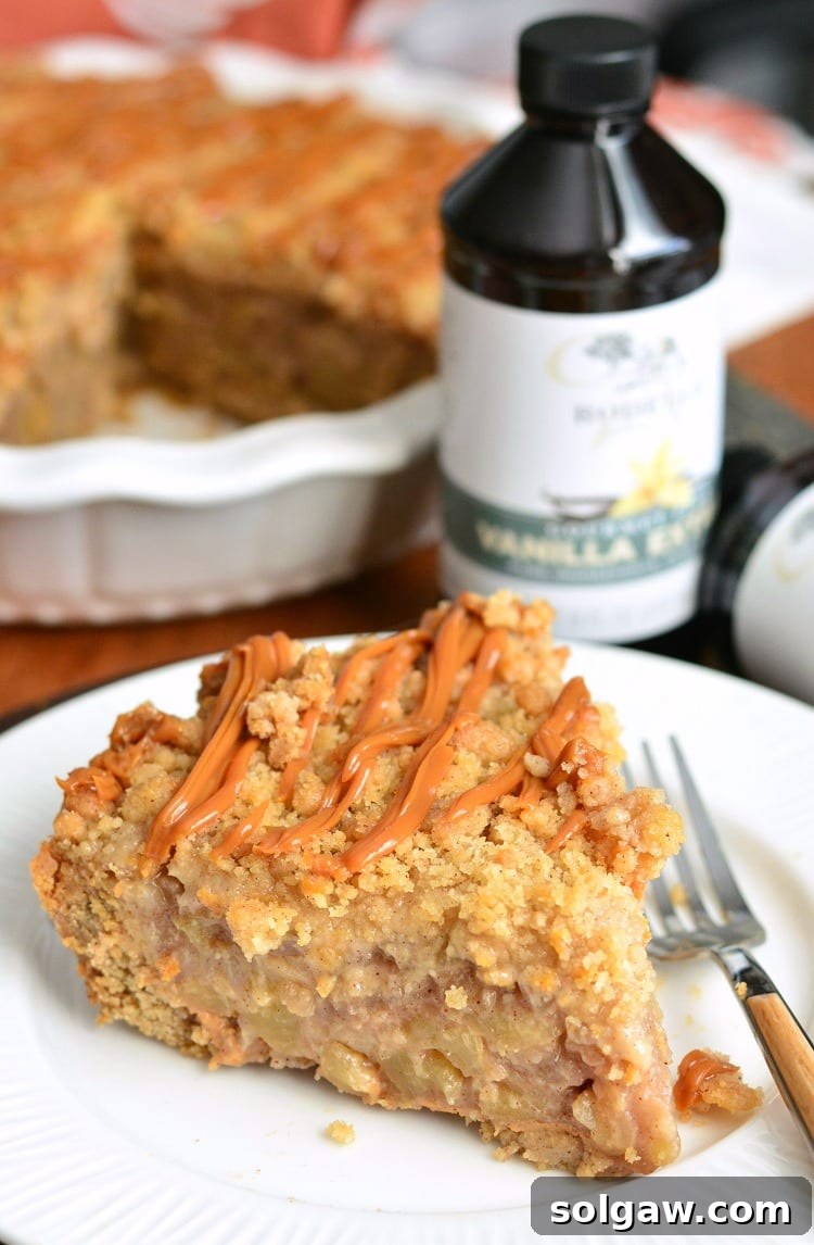 A beautifully presented slice of Caramel Apple Cookie Crust Pie on a plate, with a fork. In the background, the rest of the pie sits in its pan, alongside a bottle of Rodelle vanilla, emphasizing the quality ingredients used in the recipe.