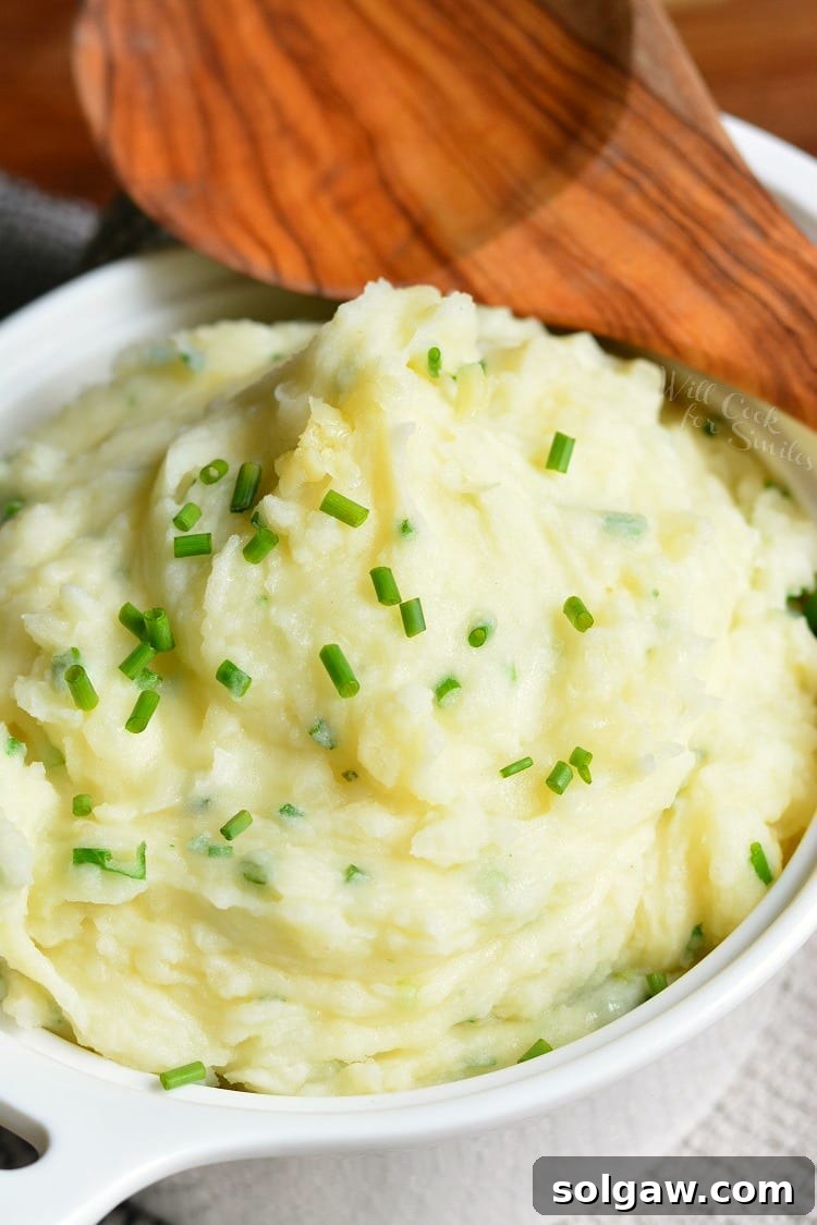 Serving bowl filled with creamy White Cheddar and Chive Mashed Potatoes, with a wooden serving spoon resting in the dish