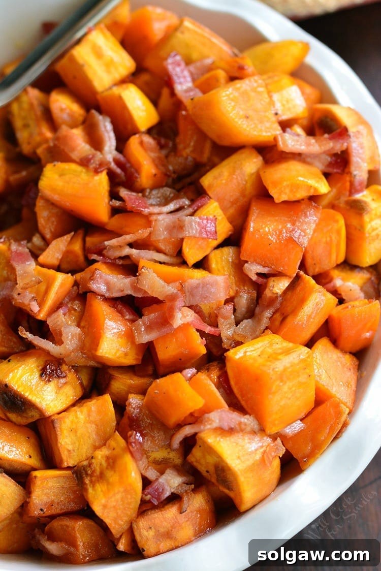 Maple Bacon Roasted Sweet Potatoes in a rustic serving bowl on a wooden table, garnished with fresh herbs