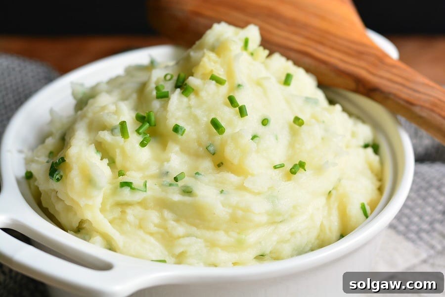White Cheddar and Chive Mashed Potatoes in a serving bowl, garnished with fresh chives
