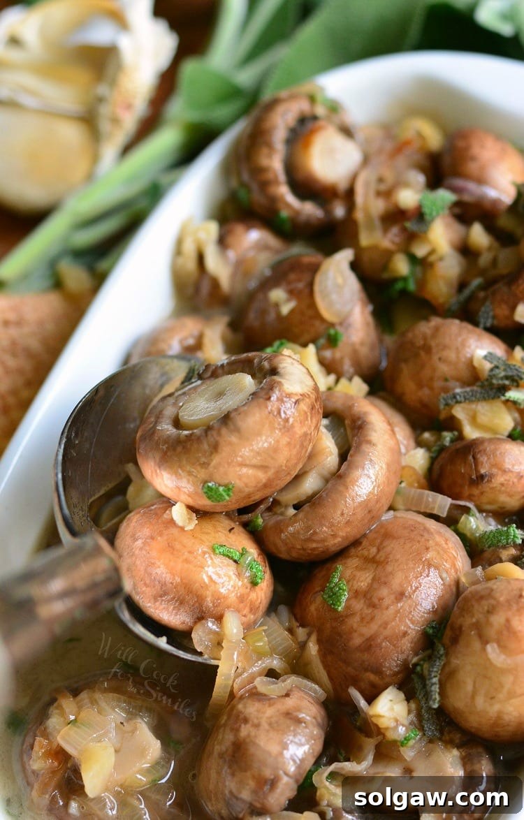 Mushrooms with Garlic and Sage in White Wine Sauce in a white baking dish with a spoon scooping some out on a cutting board with garlic in the background.