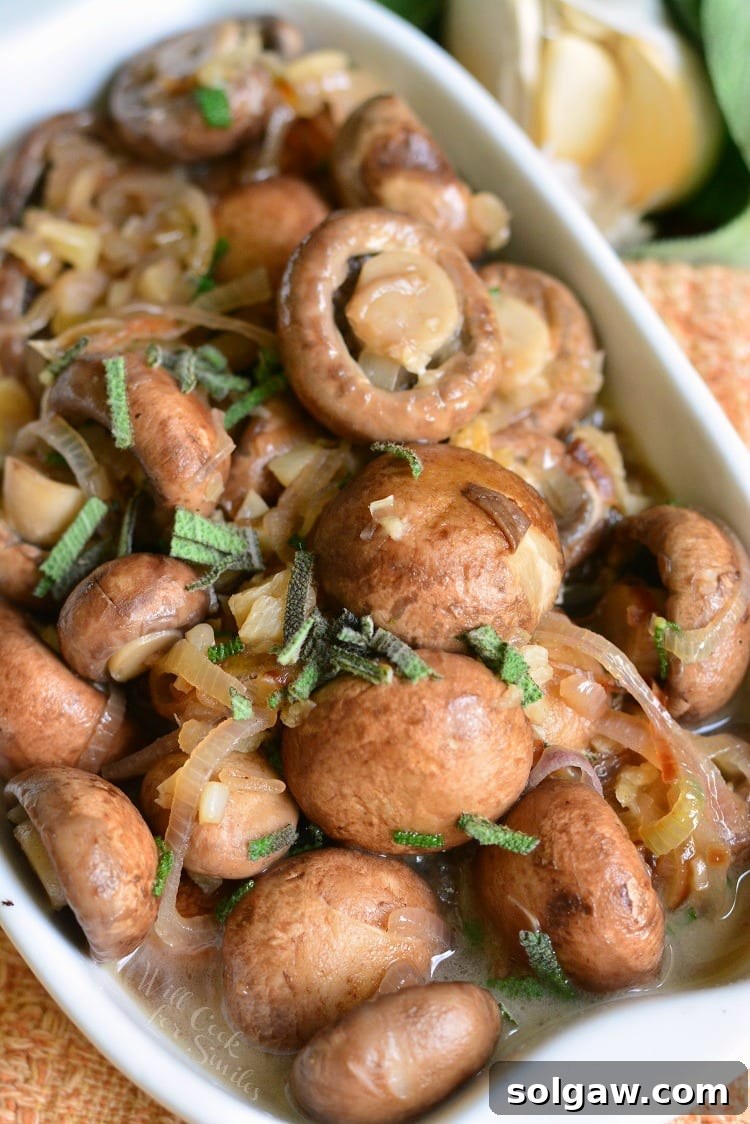 Mushrooms with Garlic and Sage in White Wine Sauce in a white baking dish on a cutting board with garlic in the background.