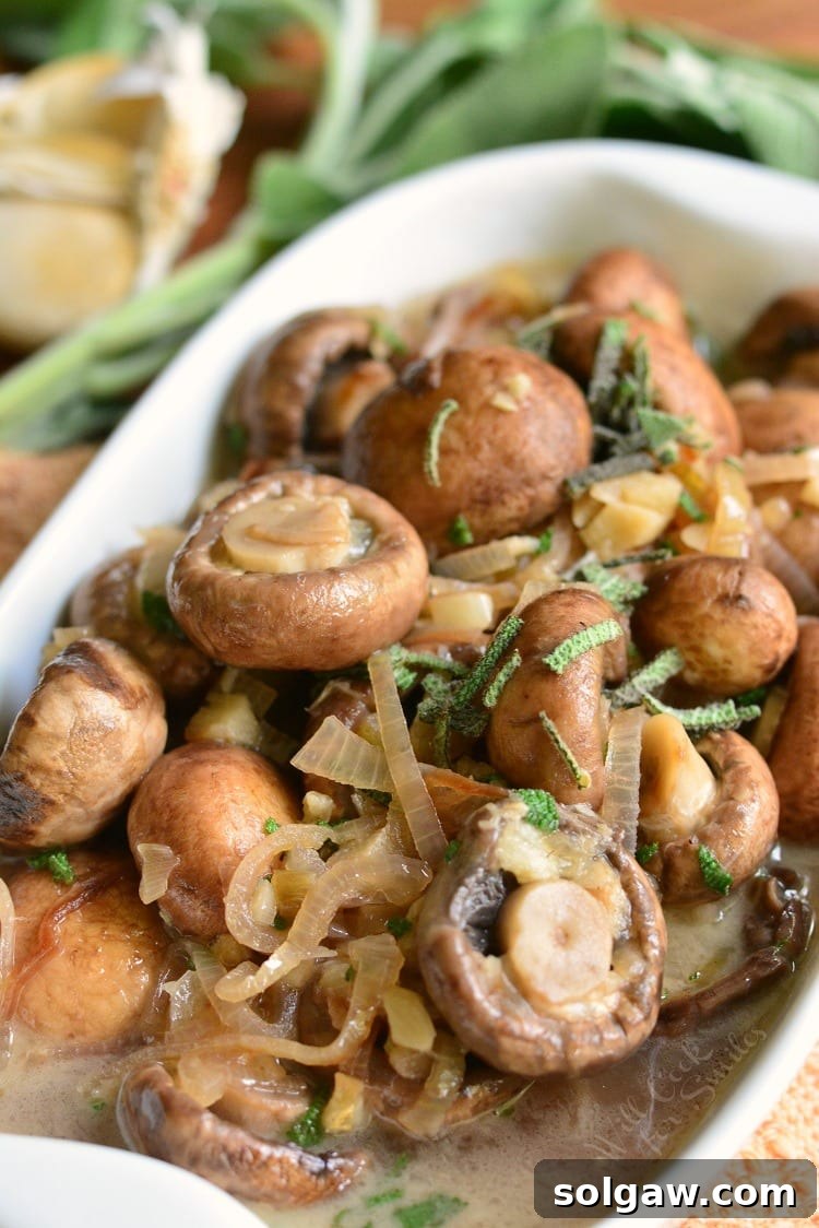 Mushrooms with Garlic and Sage in White Wine Sauce in a white baking dish on a cutting board with garlic in the background.