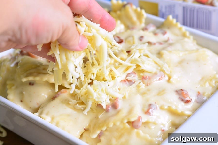 Golden-Baked Ravioli Mac with Crispy Bacon 4 sprinkling cheese over Ravioli Mac and Cheese with Bacon that is in a white casserole dish