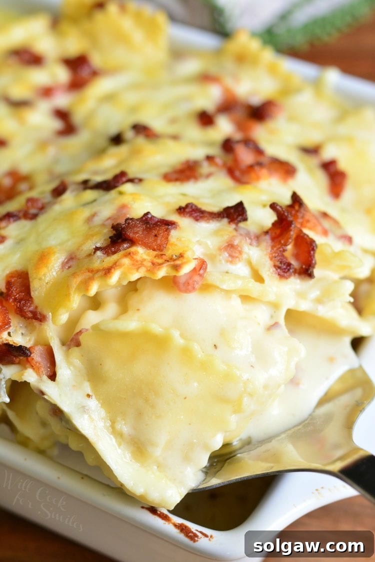 Golden-Baked Ravioli Mac with Crispy Bacon 7 spooning out Baked Ravioli Mac and Cheese with Bacon in a white casserole dish on wood table