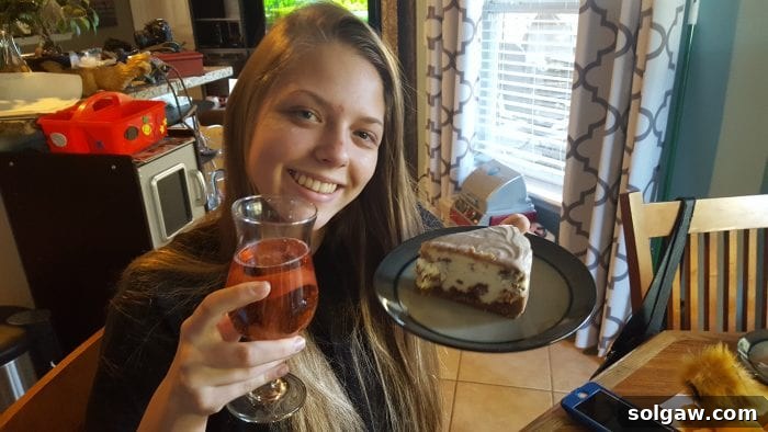 My sister excitedly holding a plate with a slice of the Cinnamon Roll Cheesecake in one hand and a drink in the other, clearly enjoying her birthday treat.