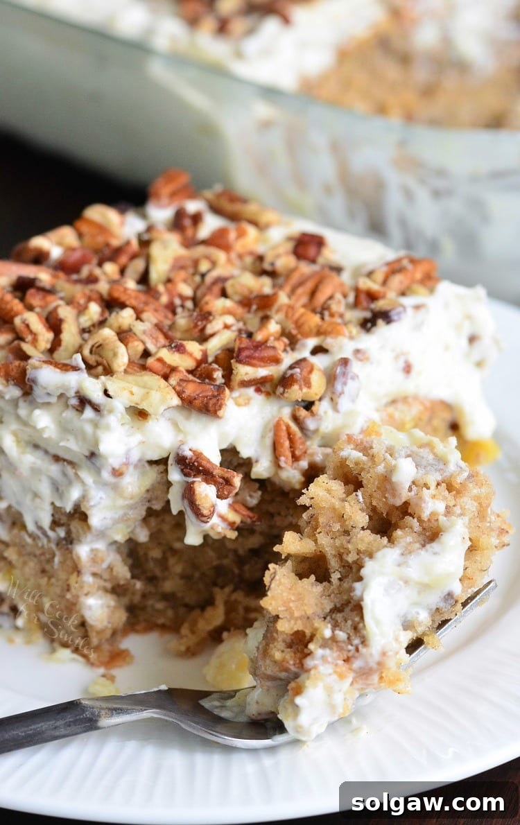 A slice of Hummingbird Poke Cake with a fork, showing the tropical fruit and pecan flavors.