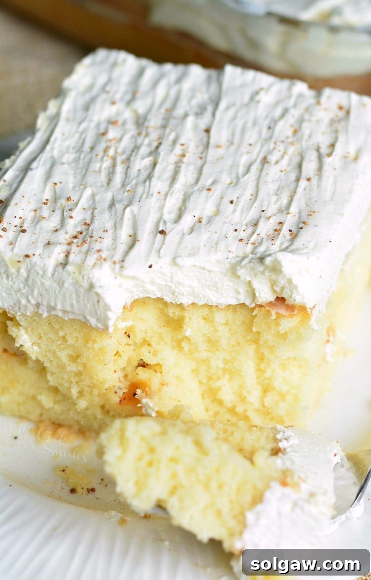 A slice of Eggnog Poke Cake on a plate with a fork, showing the moist interior soaked in sauce.