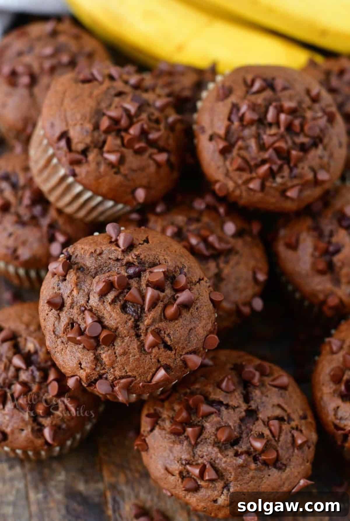 Several chocolate banana muffins stacked together next to bananas.