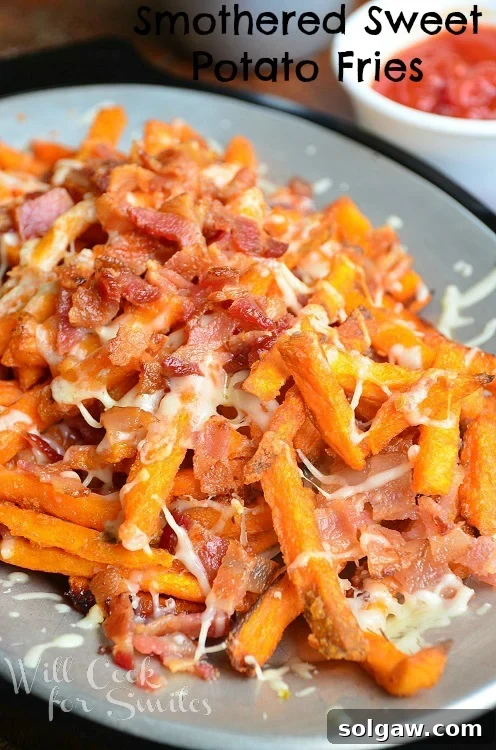 Close-up shot of perfectly smothered sweet potato fries, generously topped with melted pepper jack cheese and crispy bacon, with a dipping sauce cup in the background
