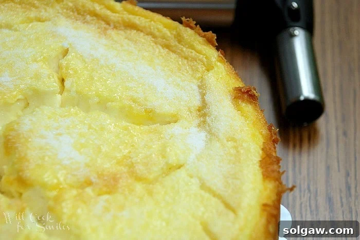 Close-up of a Crème Brûlée Layered Cheesecake, with a cooking torch held to the side, ready to caramelize the sugar topping to perfection.