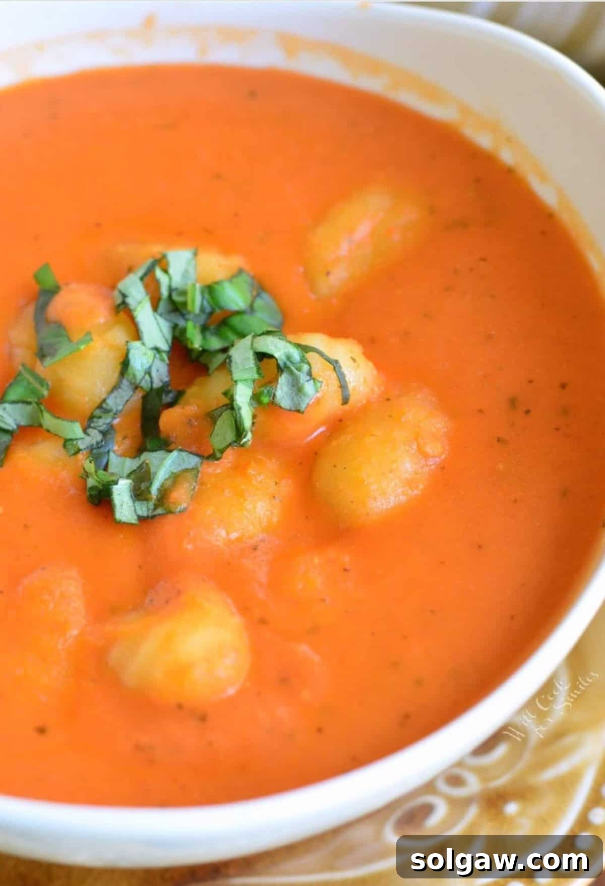 Tomato soup with gnocchi in a bowl with a spoon and basil sprinkled on top as garnish.
