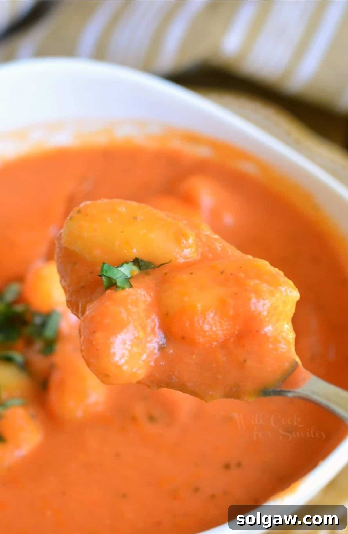 Homemade tomato soup with gnocchi scooped on a spoon from a bowl.