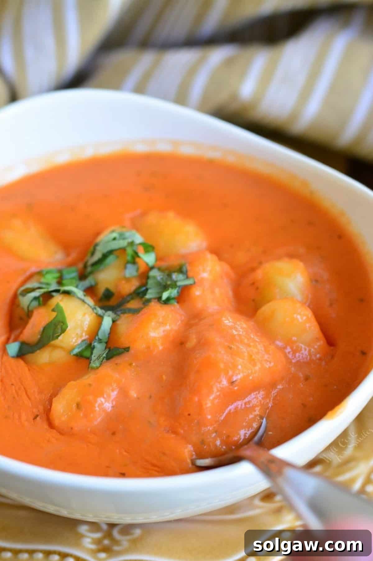 Tomato soup with gnocchi in a bowl with a spoon scooping some out.