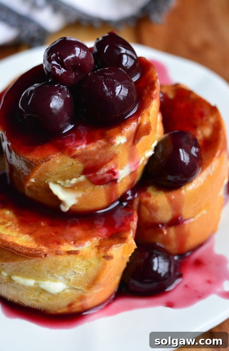 Stacked cherry cheesecake stuffed french toast on a plate, garnished with fresh cherries and a dusting of powdered sugar.