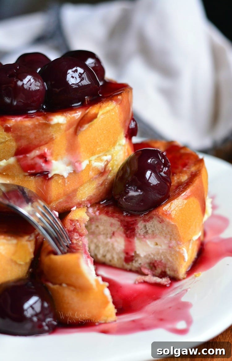 Golden brown cherry stuffed french toast with a spoonful of brandy cherry sauce and fresh cherries on top.