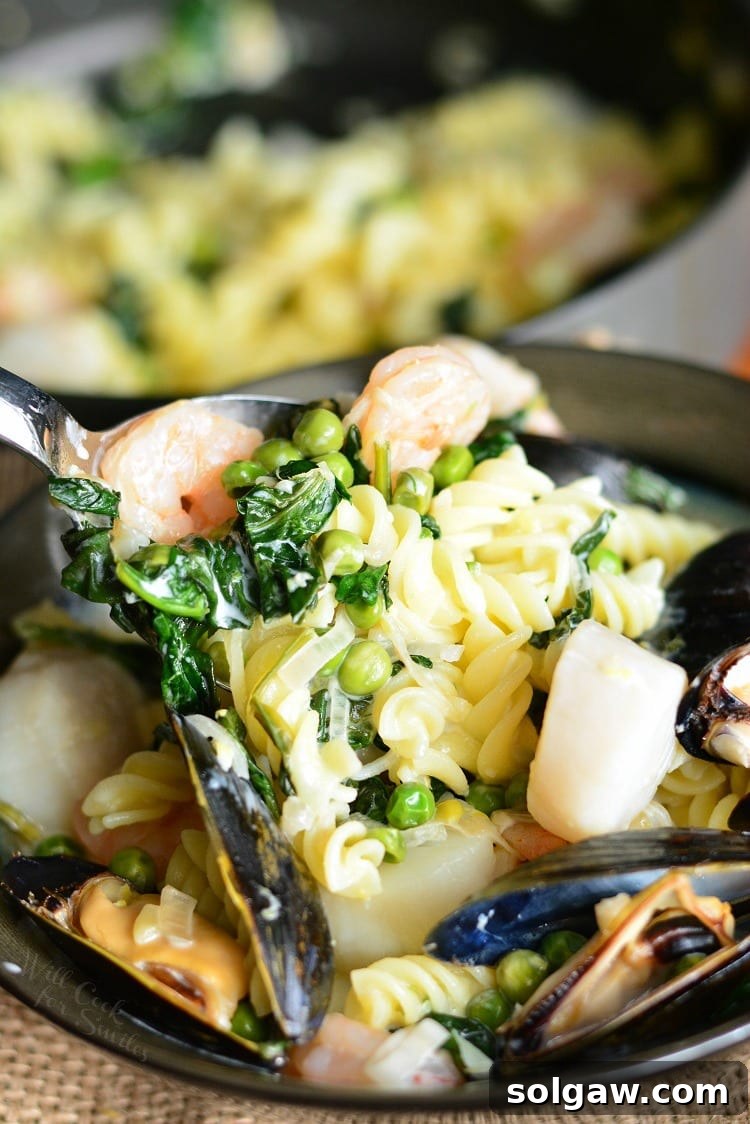Close-up of Creamy Spinach and Peas Seafood Pasta in a pan with a spoon lifting some out, showcasing the creamy sauce and fresh ingredients