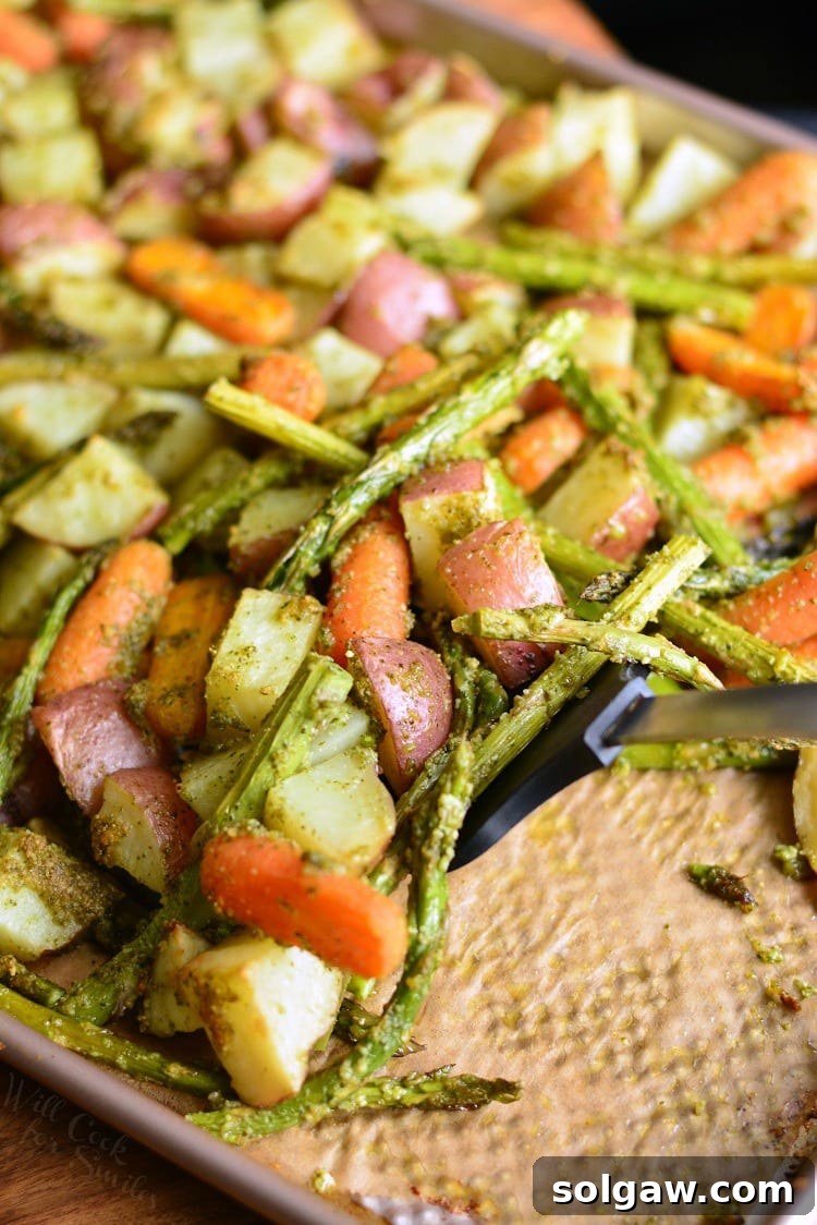 Pesto Roasted Potatoes Carrots and Asparagus on a baking sheet with a spatula 