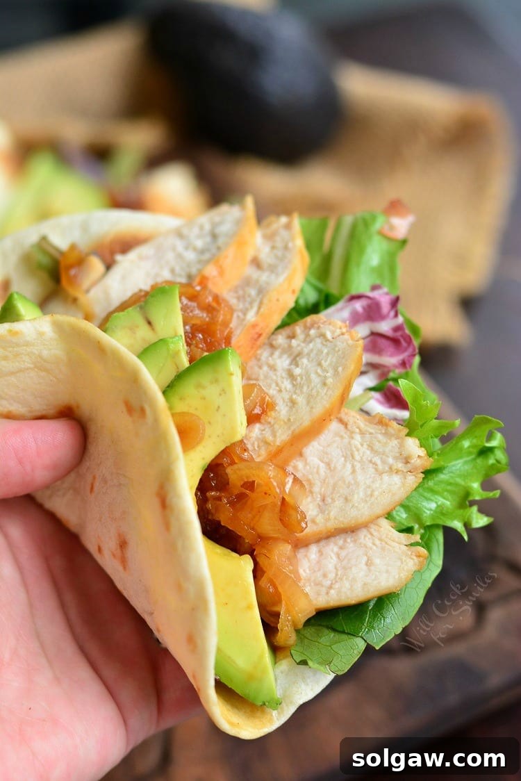 A hand holding a vibrant chicken taco filled with marinated chicken, fresh lettuce, and creamy avocado slices.