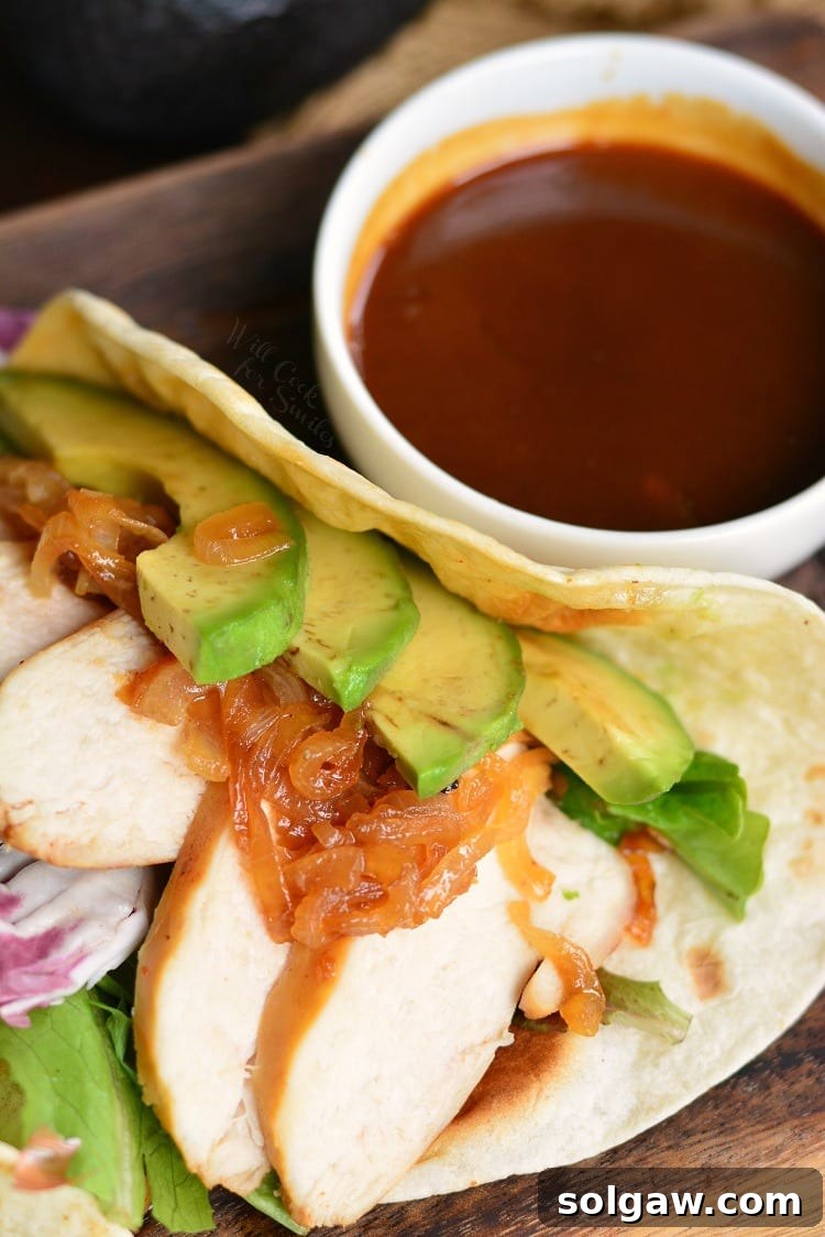 A close-up view of a perfectly assembled chicken taco with avocado slices and a bowl of the reduced tequila sauce on the side.