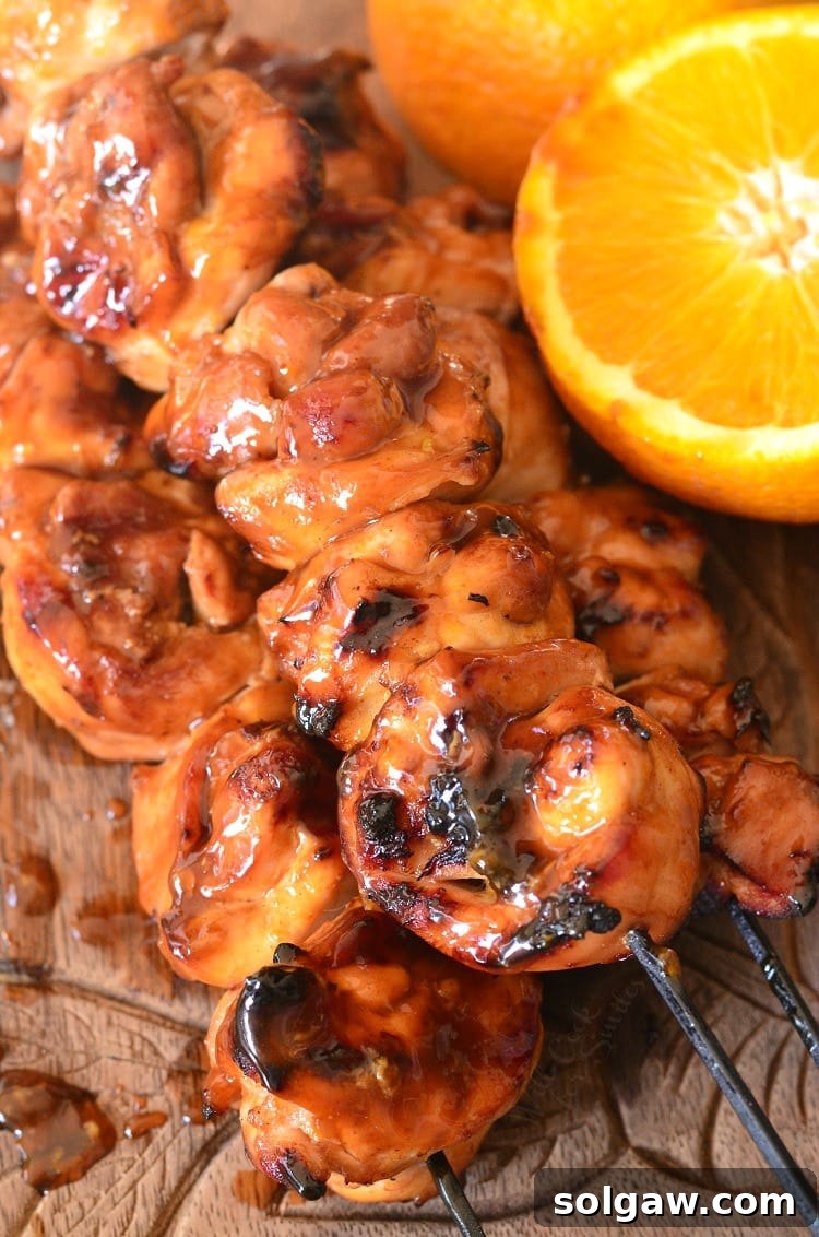 Sticky Orange Chicken Kebabs on a wood cutting board with a orange that is sliced in half