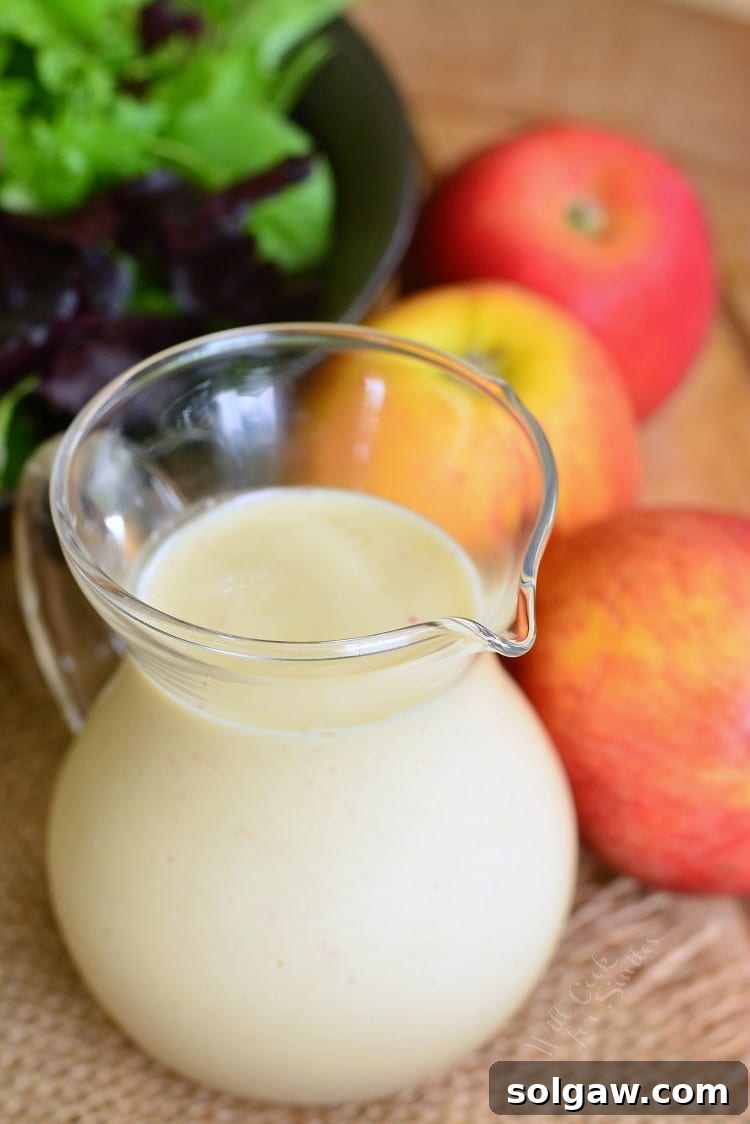 Delicious homemade Apple Vinaigrette in a glass container on a wood table with apples and salad in the background