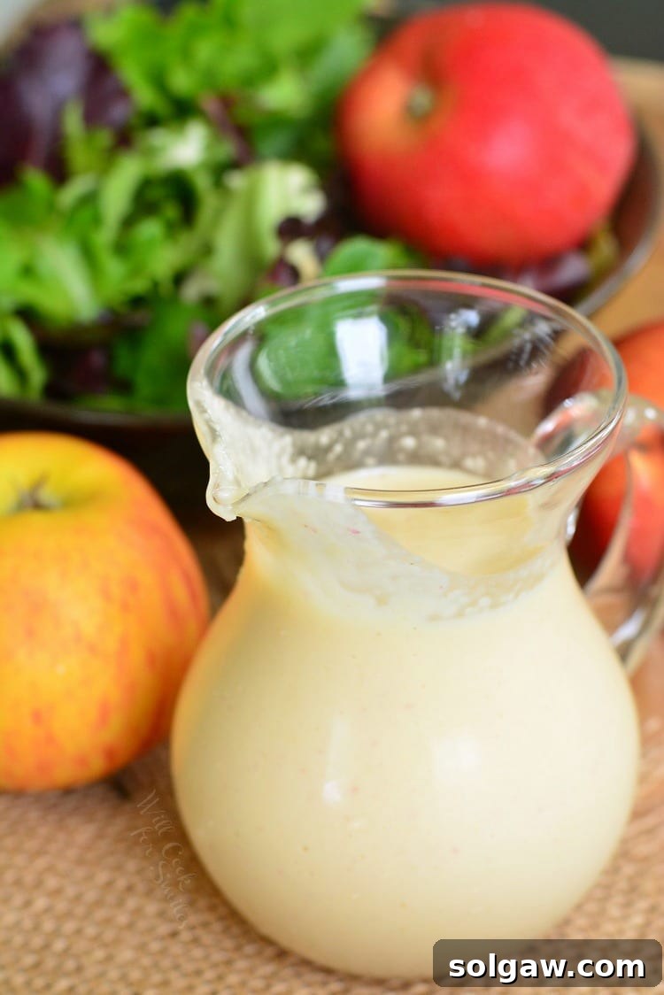 Delicious homemade Apple Vinaigrette in a glass container on a wood table with apples and salad in the background