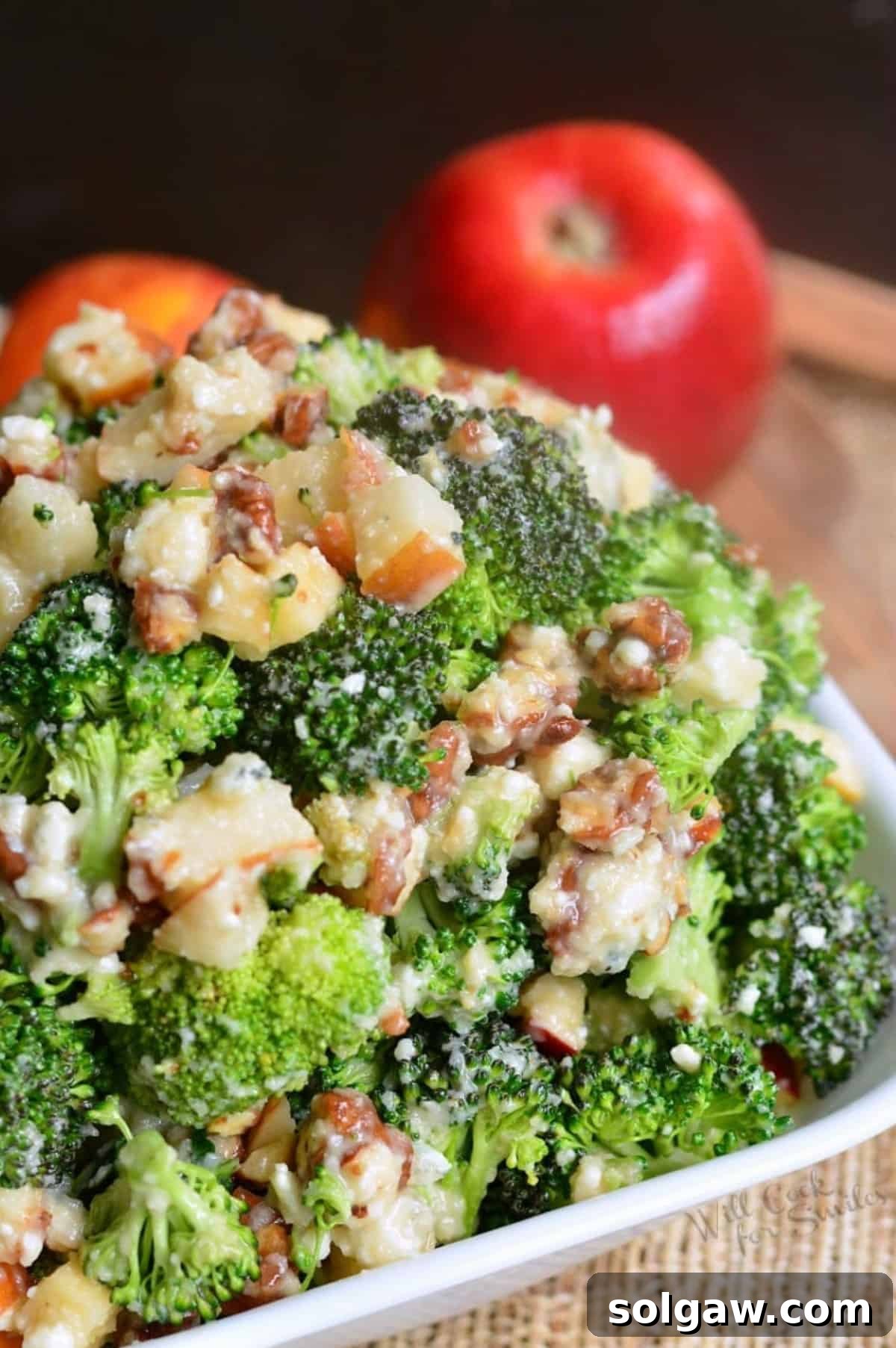 A vibrant bowl full of refreshing broccoli salad, richly mixed with pecans, sweet pears, crisp apples, and tangy blue cheese crumbles, perfect for a summer gathering.