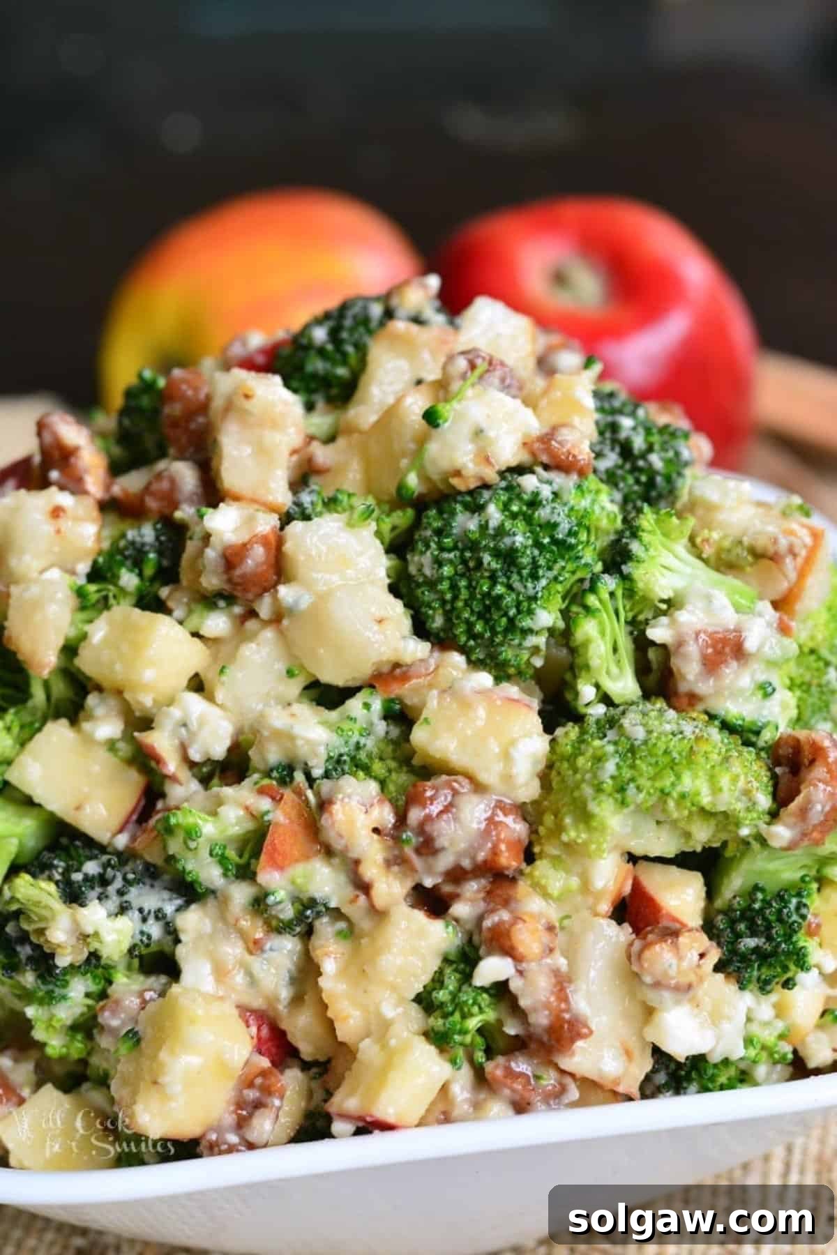 A crisp white bowl generously filled with a vibrant Pear Apple Broccoli Salad, featuring prominent pieces of apple, crunchy nuts, and savory blue cheese, all tossed together.