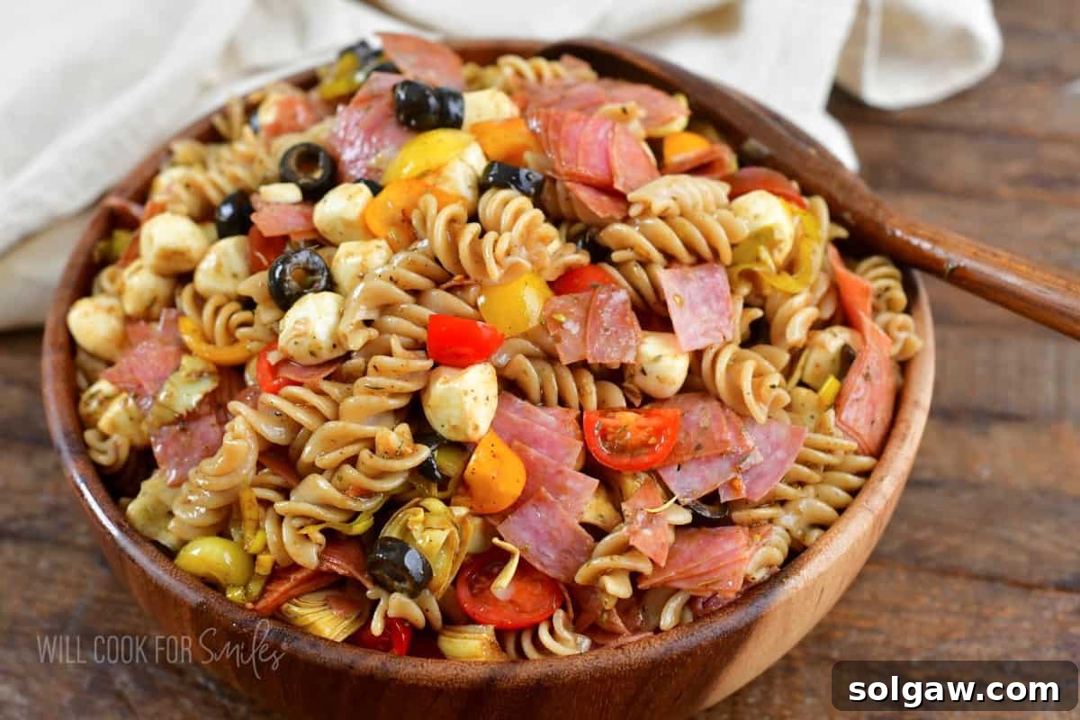 Antipasto pasta salad in a wooden salad bowl with a wooden spoon.
