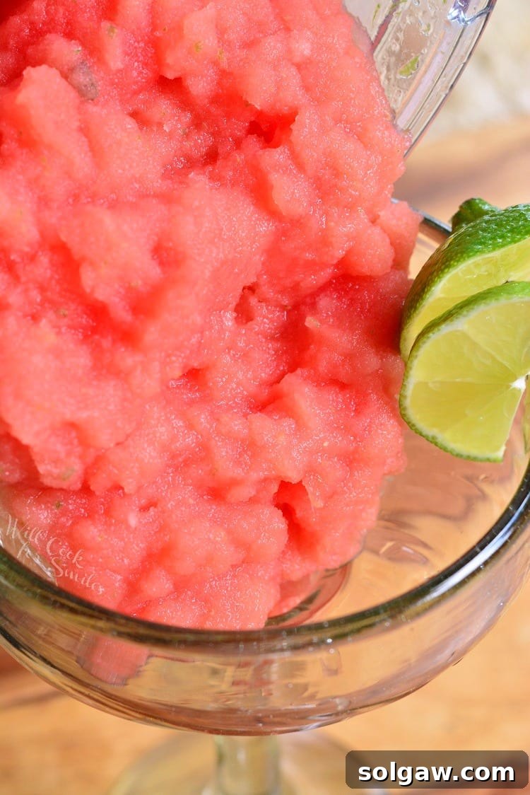 A vibrant red frozen watermelon margarita being poured into a salt-rimmed glass, showing its smooth, icy texture.