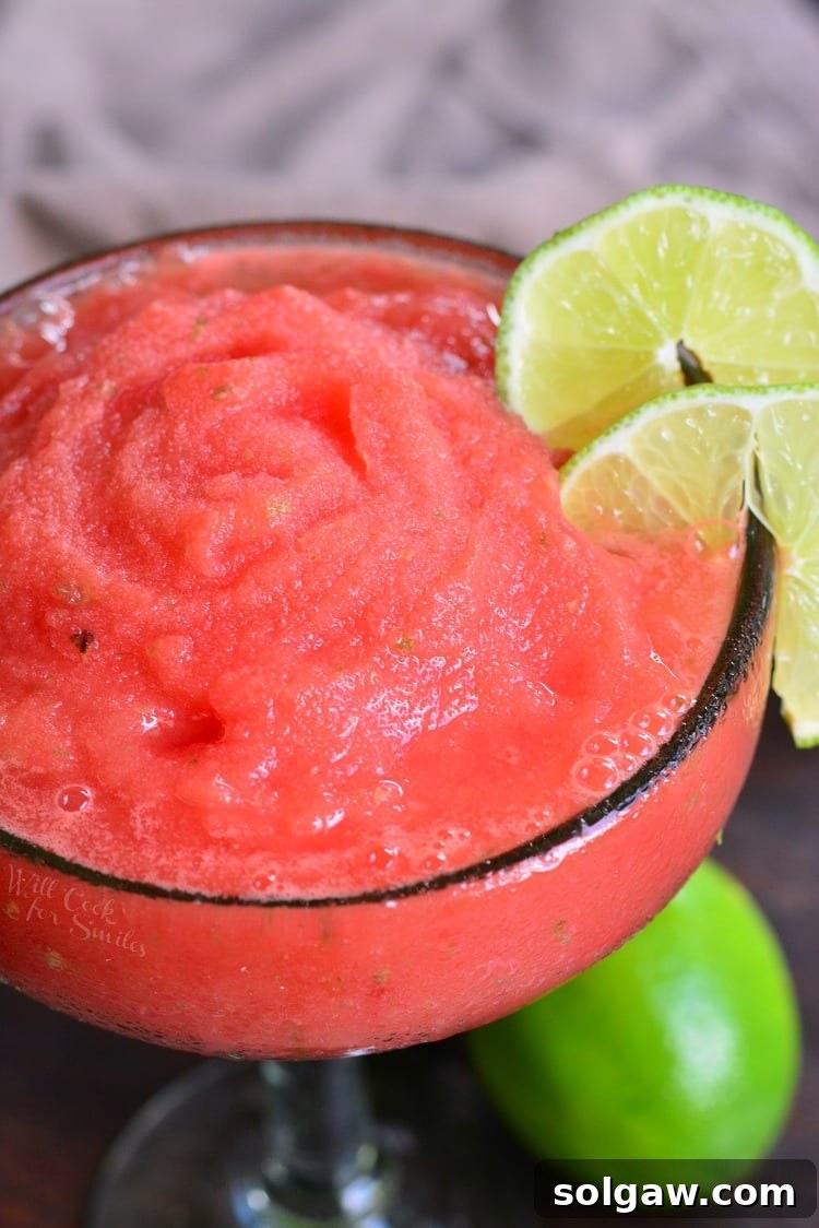 Overhead shot of a beautifully garnished frozen watermelon margarita, surrounded by fresh lime slices and small watermelon cubes, inviting for a refreshing sip.
