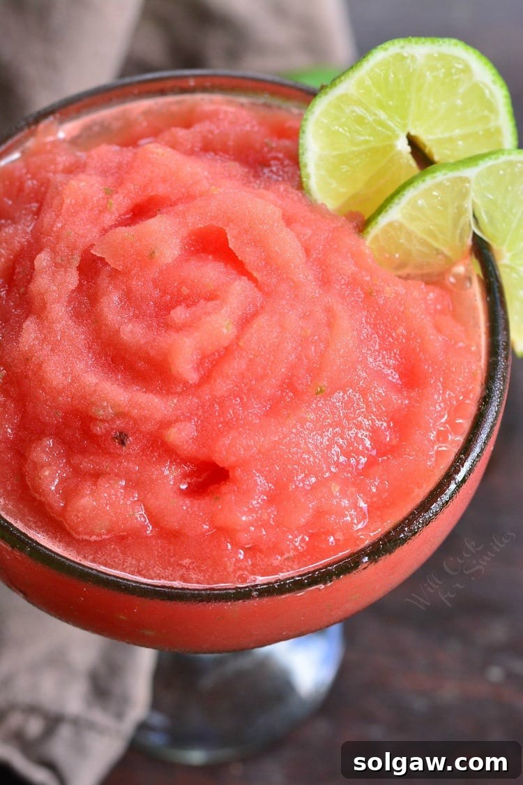 Top of a frozen margarita in a glass with lime wedges as garnish.