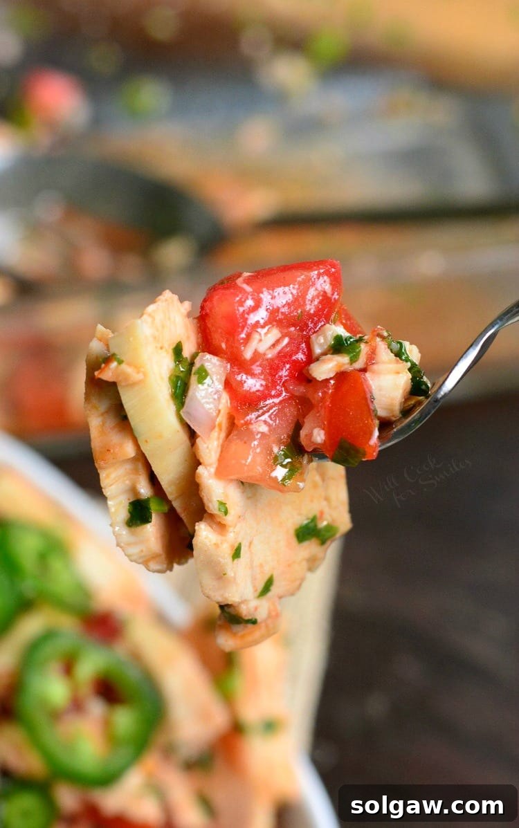 Close-up of a fork holding a bite of Spicy Mexican Chicken Salad, showcasing the delicious blend of chicken, tomatoes, and cilantro