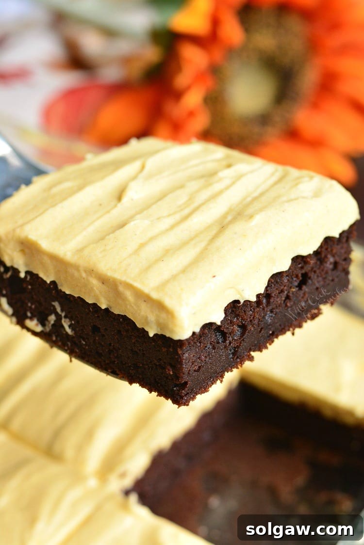 Frosted Pumpkin Brownies being lifted out of a baking pan, showing the thick layer of frosting.