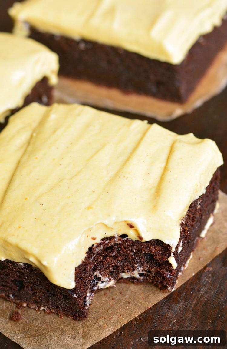 Frosted Pumpkin Brownies on parchment paper, with a slice removed, revealing the soft layers.