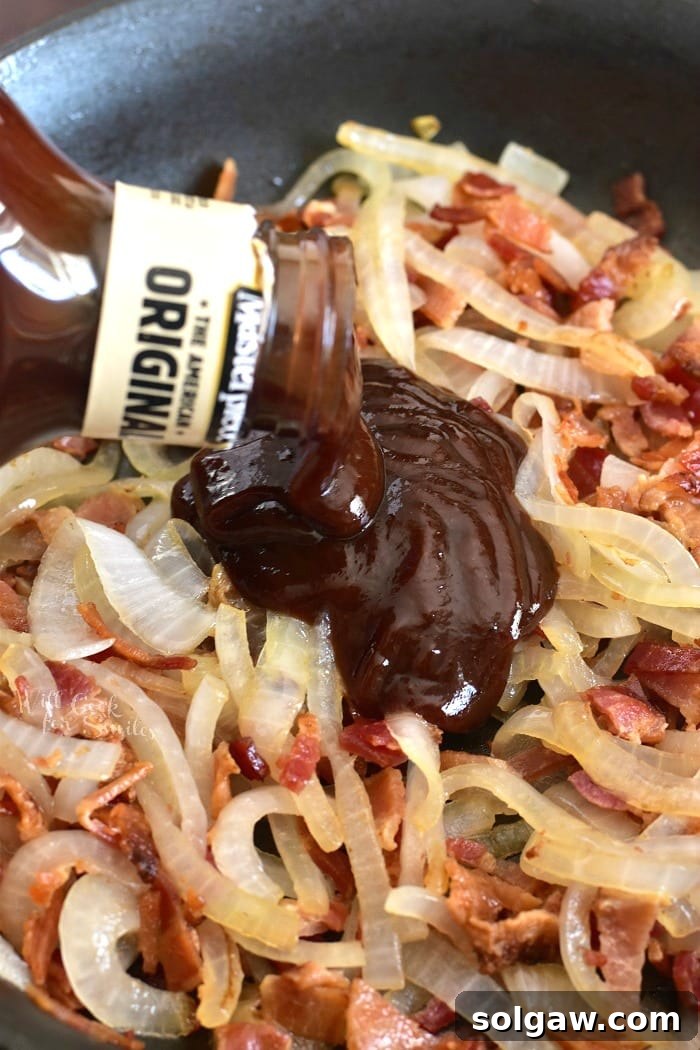 A delicious mixture of cooked onions and bacon being combined with tangy BBQ sauce in a pan