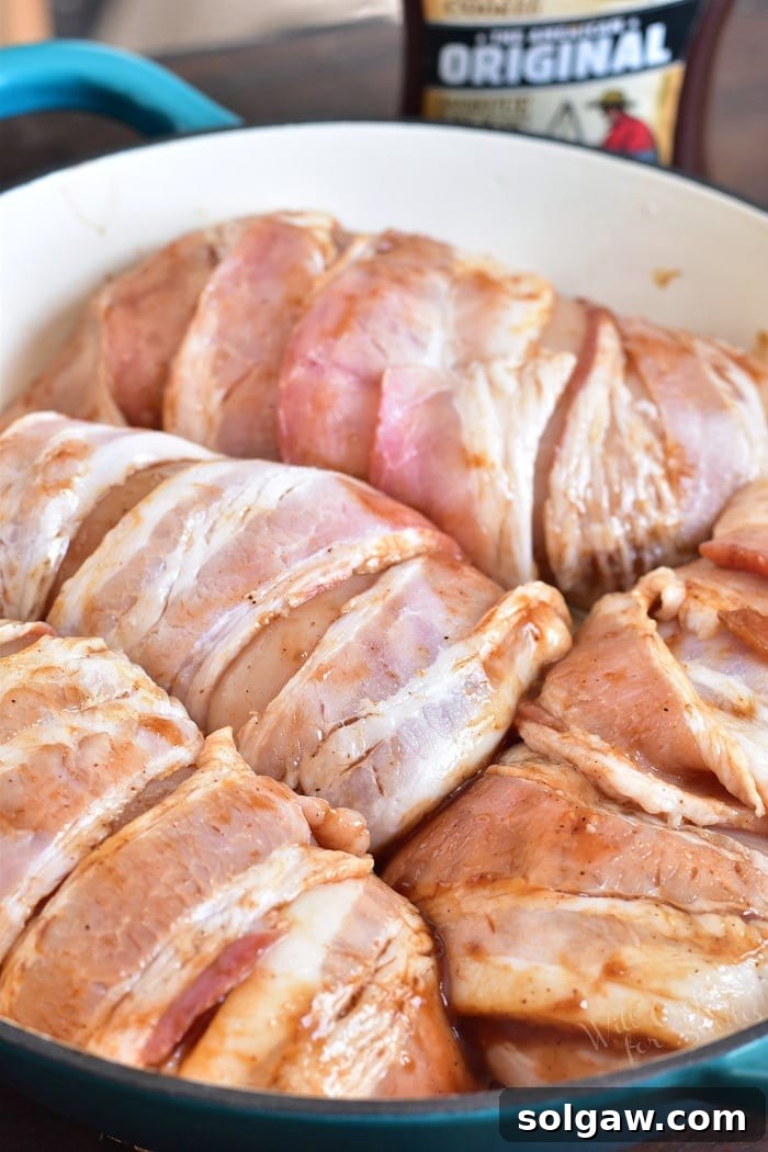 Raw chicken breasts, expertly wrapped in strips of bacon, placed in an oven-safe pan, ready for searing and baking.