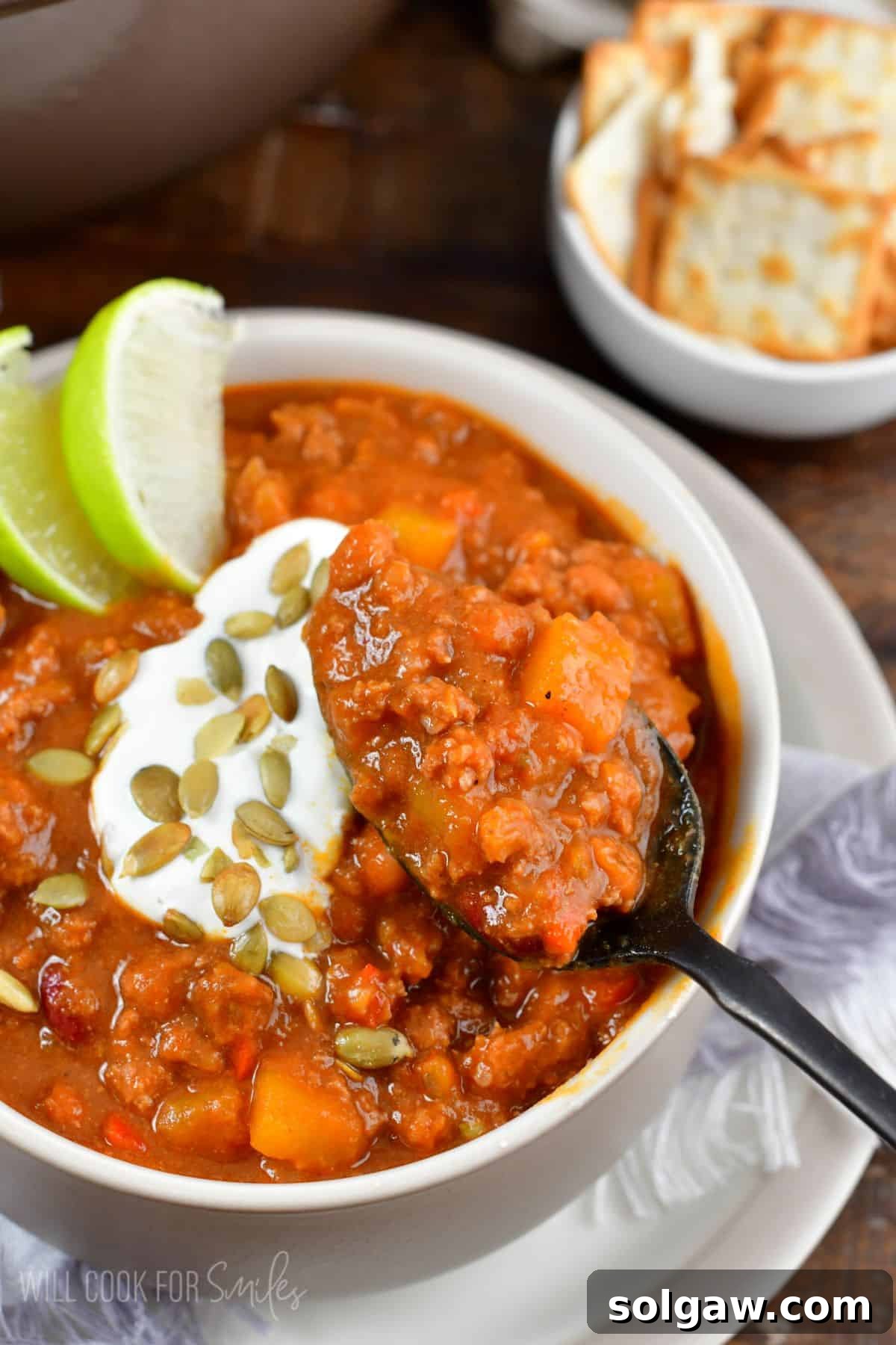 A bowl of rich pumpkin chili, garnished with pumpkin seeds, sour cream, and a lime wedge, ready to be served.