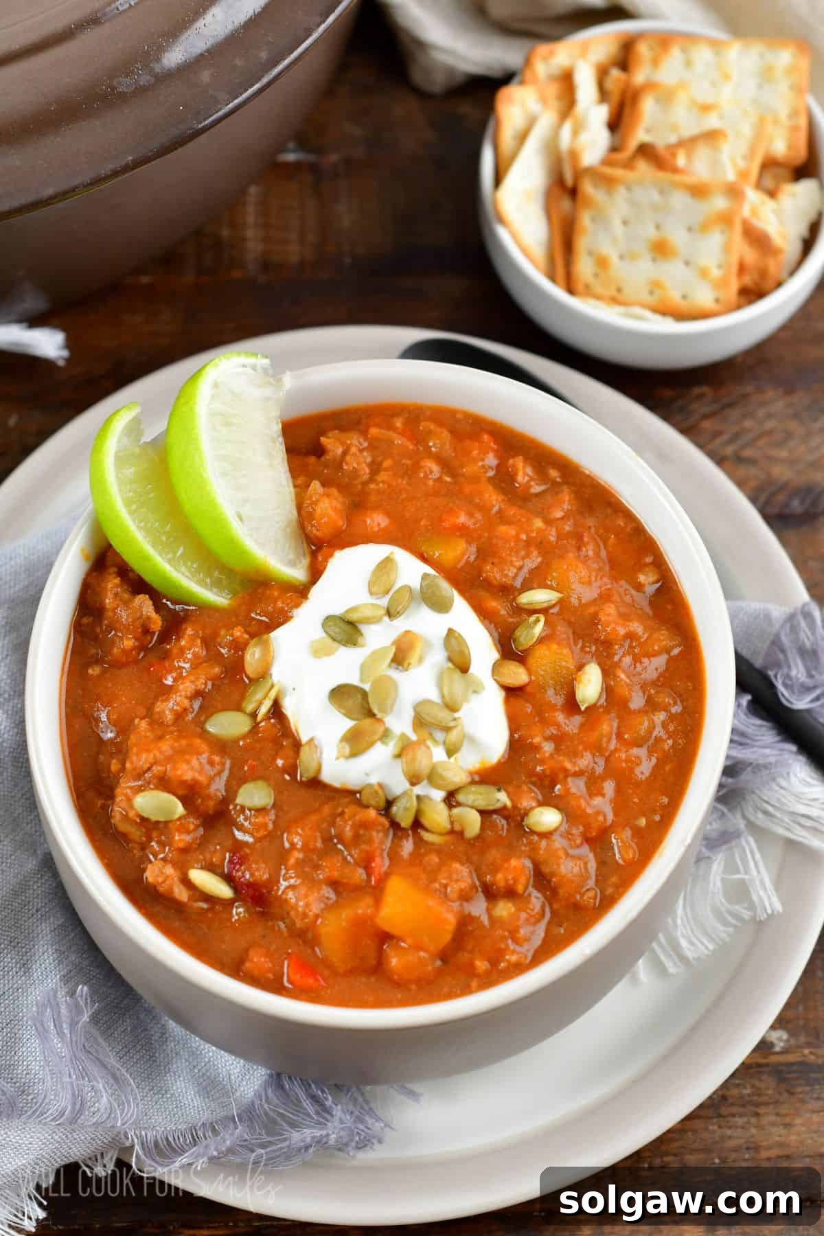 A close-up shot of a bowl of pumpkin chili with sour cream, pumpkin seeds, and a lime wedge garnish, highlighting the rich texture.