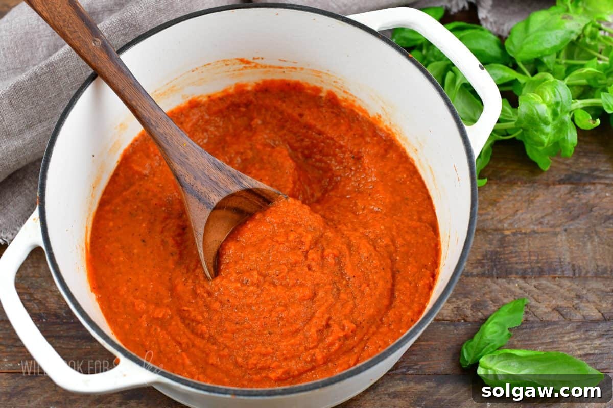 A pot of freshly made homemade spaghetti sauce, garnished with fresh basil leaves, with a wooden spoon resting inside, all on a rustic wooden surface.