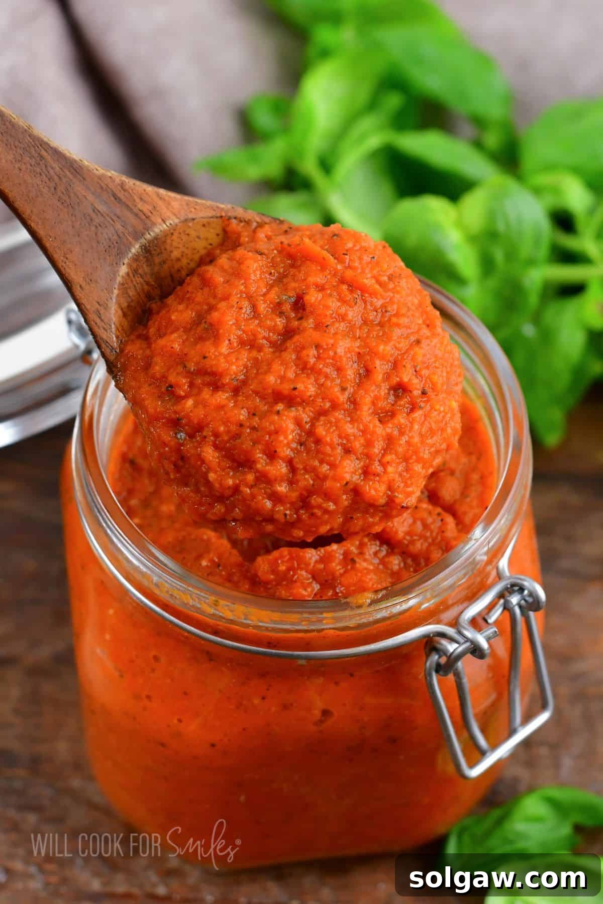 A glass jar of homemade spaghetti sauce, with a wooden spoon, ready to be served