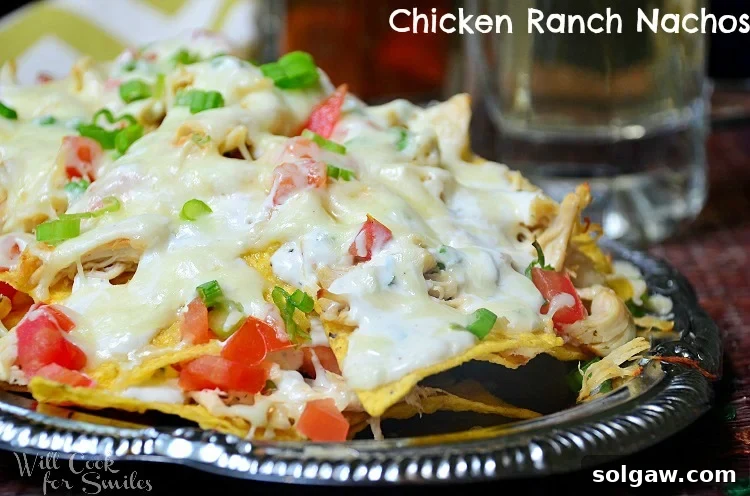 Close-up shot of golden-baked Chicken Ranch nachos on a metal platter, showcasing melted cheese and fresh toppings.