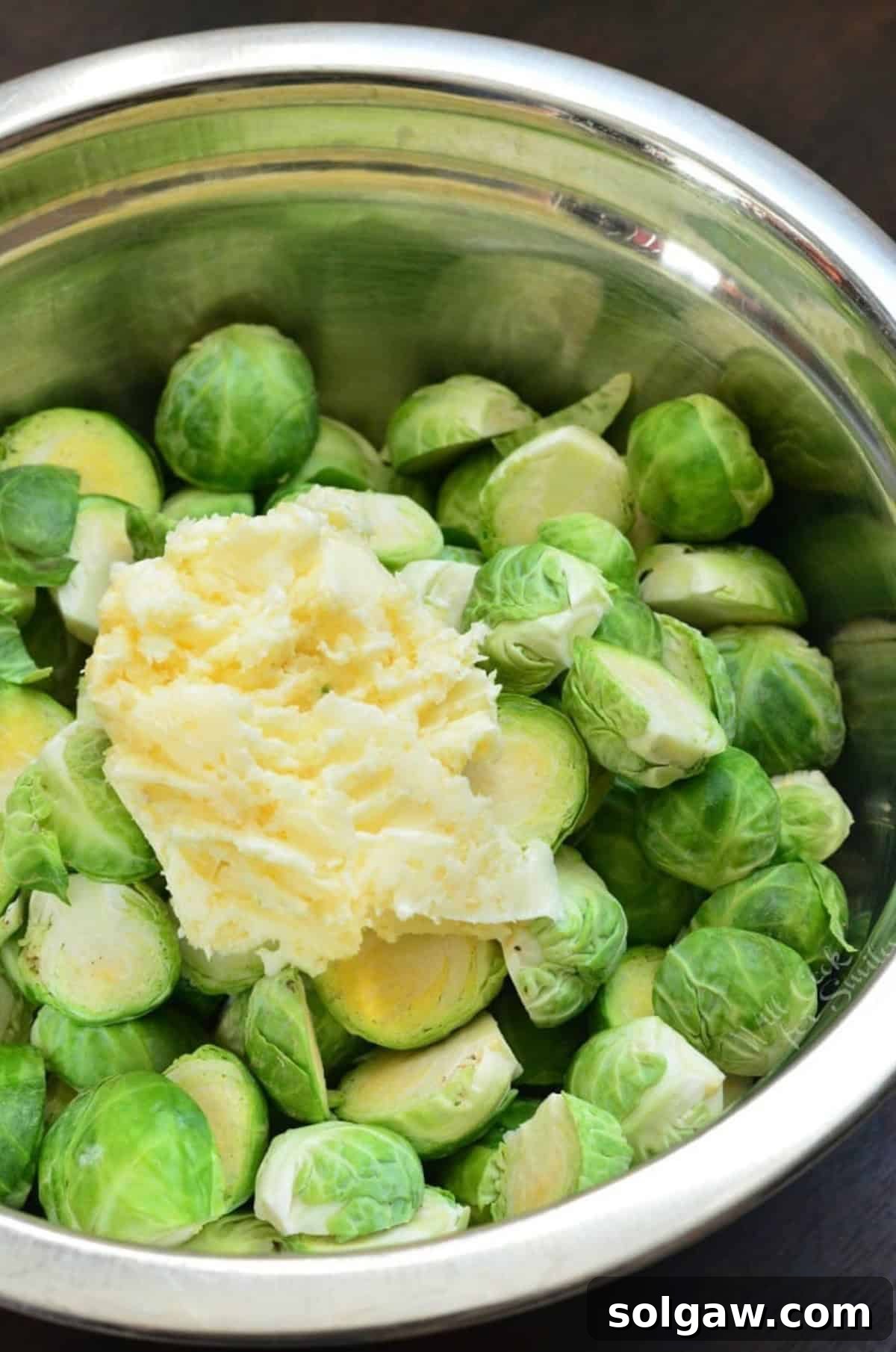 A metal bowl of brussel sprouts with garlic butter on top.