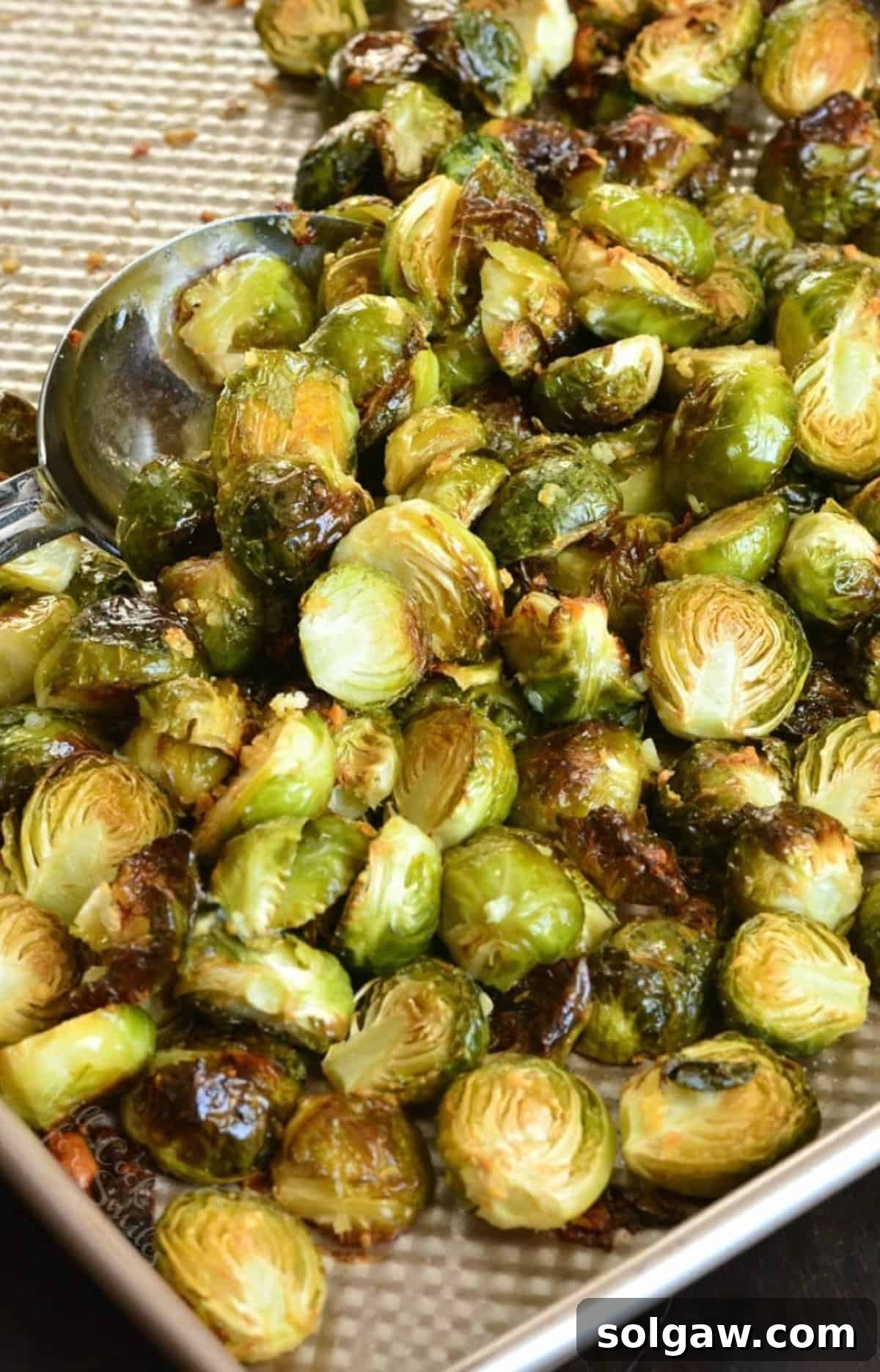 Garlilc butter roasted brussels sprouts on a baking sheet with a metal serving spoon scooping some up.