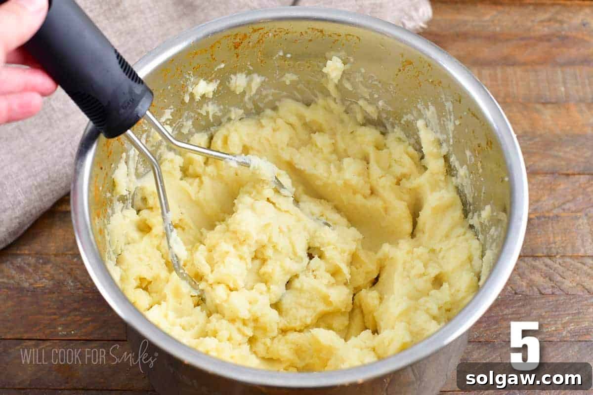 A close-up shot of rich, fluffy mashed potatoes being expertly mashed directly in the Instant Pot's inner bowl with a hand masher.